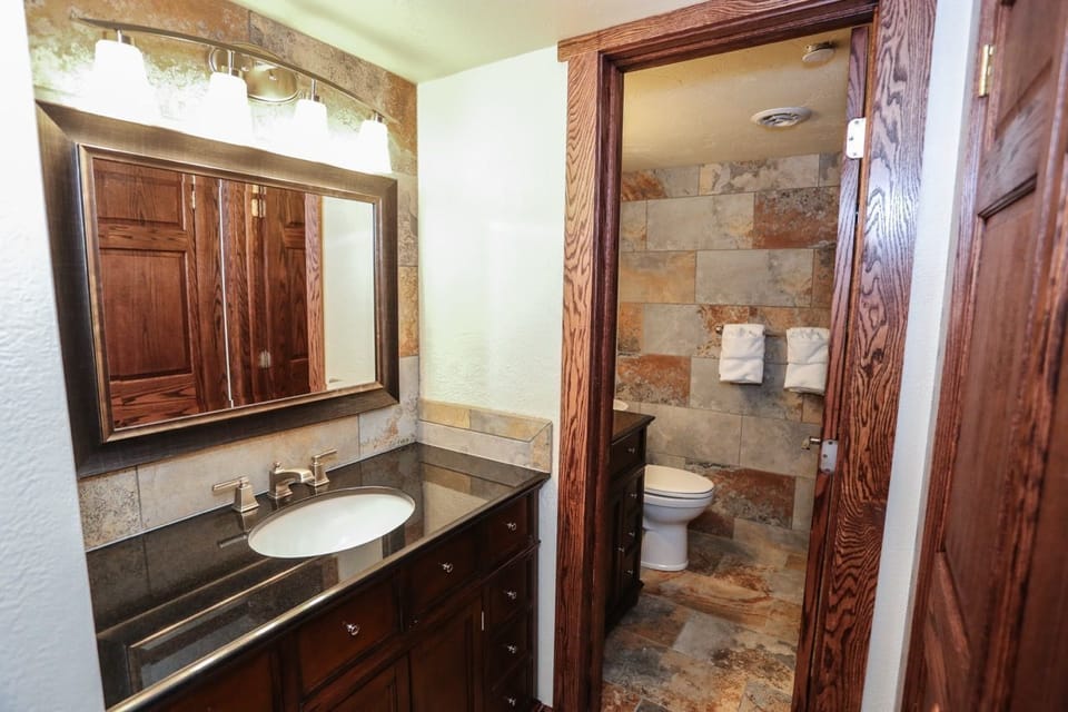 Elegant bathroom with rich wood cabinetry, a spacious vanity, and a stone-tiled shower for a rustic yet refined touch.