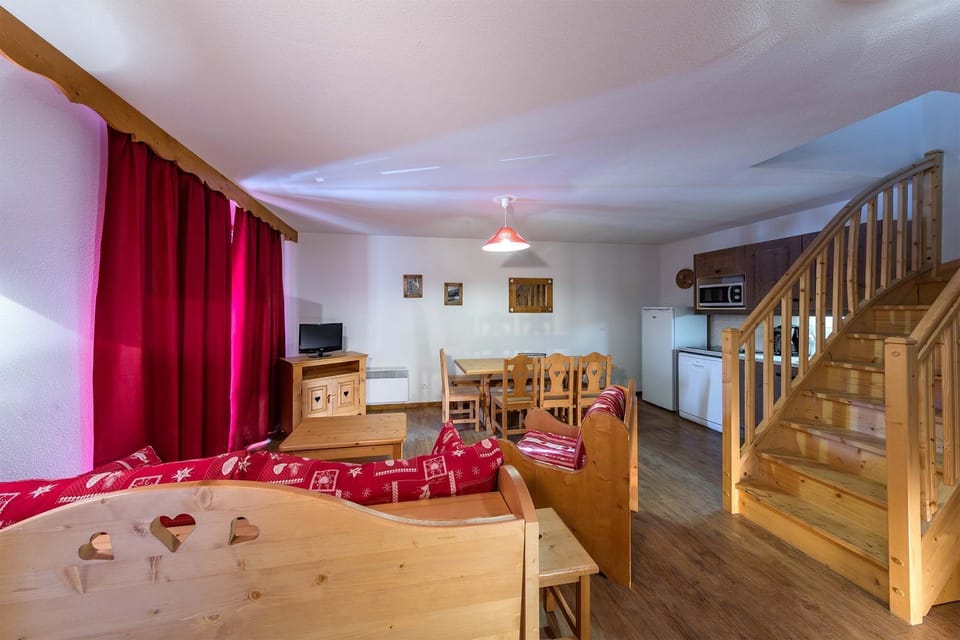 Charming duplex living space with cozy seating, a dining area, and a wooden staircase leading to the upper level.