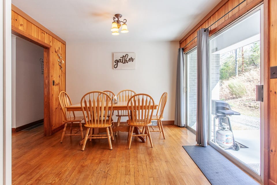 The dining area offers a rectangular wood table, spindle-back chairs, and a sliding glass door at this Bryson City rental.