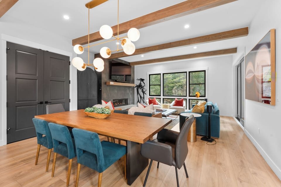 Gather around this stunning dining table beneath warm wood beams, where your group can share meals and laughter. The open layout flows seamlessly into the cozy living area with its inviting fireplace.