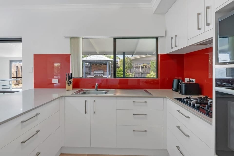 Whip up delicious meals in the fully equipped kitchen, boasting a bold red glass splashback, essential appliances, and a spacious bench with two bar stools for casual dining or morning coffee.