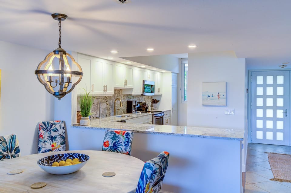 Floral-upholstered dining chairs encircle a round whitewashed table beneath an orb chandelier near the kitchen.