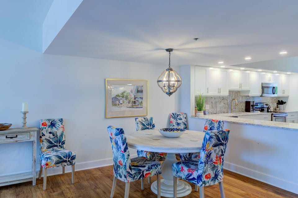 Round whitewashed dining table surrounded by floral-patterned chairs beneath a globe pendant light.
