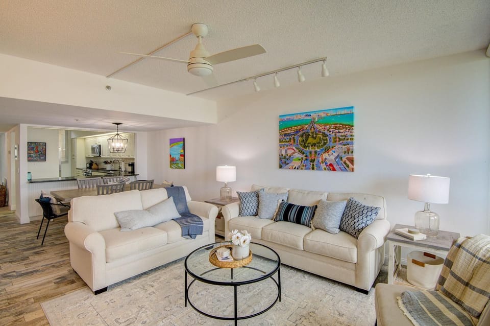 Living area with cream sofas adorned with patterned pillows, a round glass coffee table, and colorful wall art.