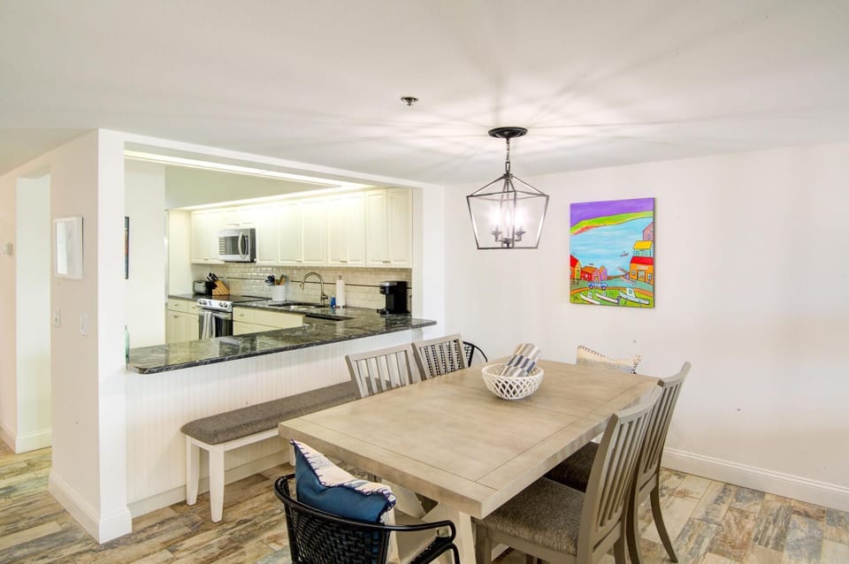 Dining area with gray wood table, mixed seating including bench and cushioned black chair, and colorful wall art.