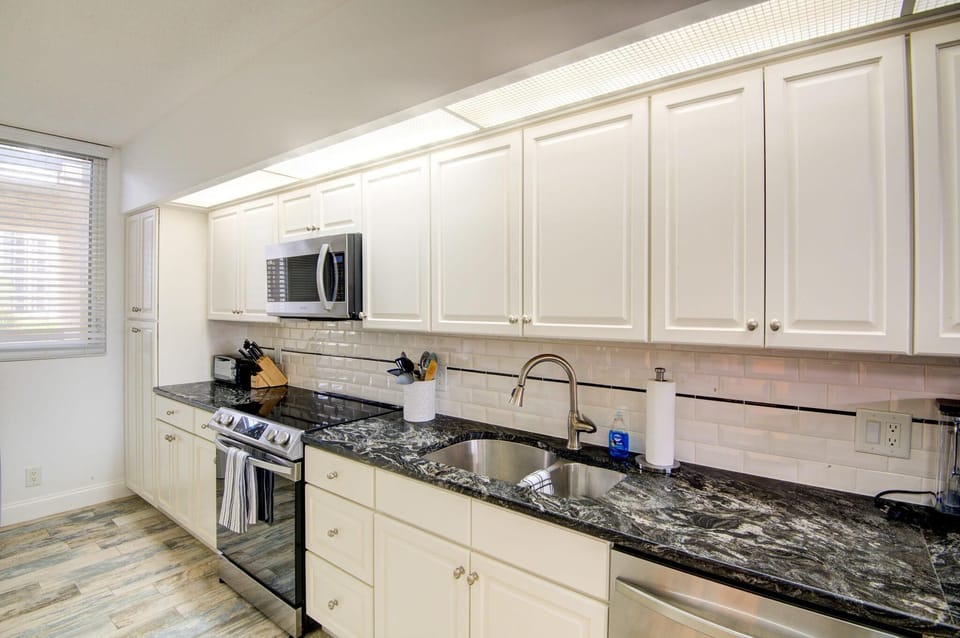Kitchen features black-and-white marbled countertops, stainless steel appliances, white cabinetry, and wood-look flooring.