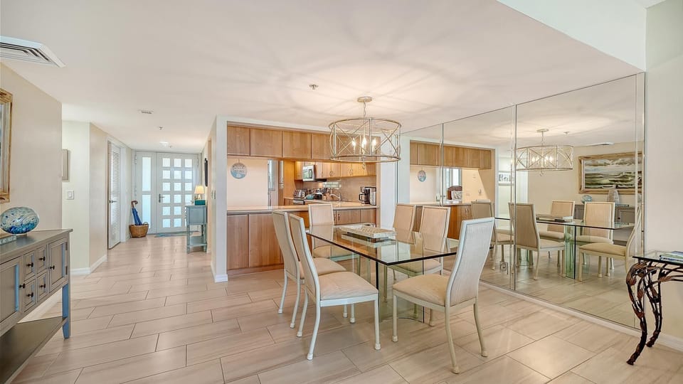 Light wood cabinetry lines the kitchen pass-through, visible beyond the dining area with tiled floors and a large mirrored wall.