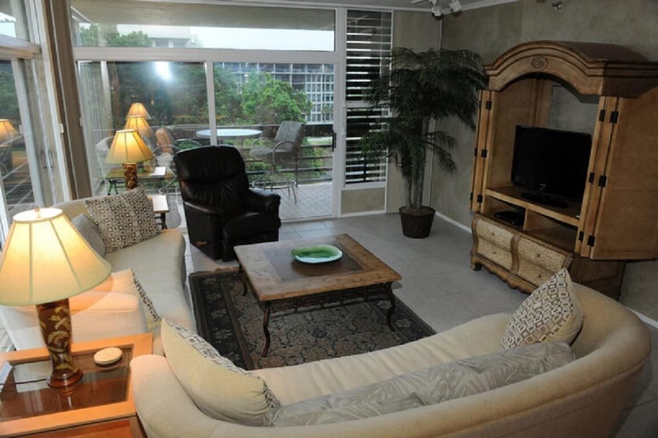 Curved beige sofa and black recliner surround a wood coffee table atop a patterned rug in the living room.