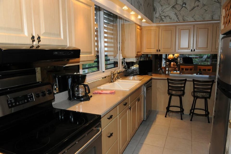 Two wrought iron bar stools sit at the kitchen counter, facing a dining area with warm lighting.