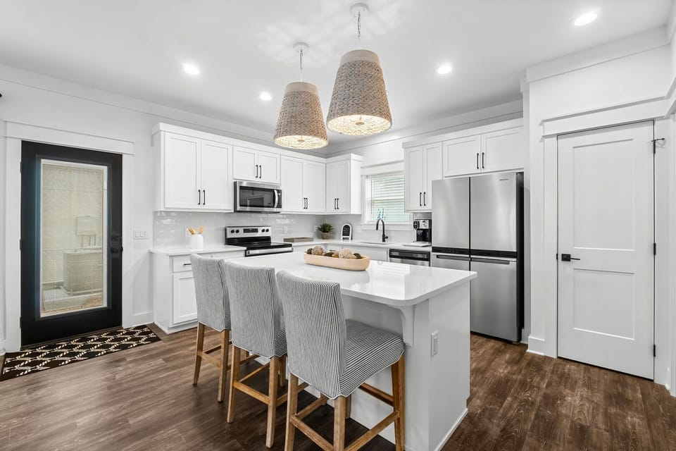 A bright and modern kitchen with white cabinetry, stainless steel appliances, a spacious island with bar seating, and stylish pendant lighting.