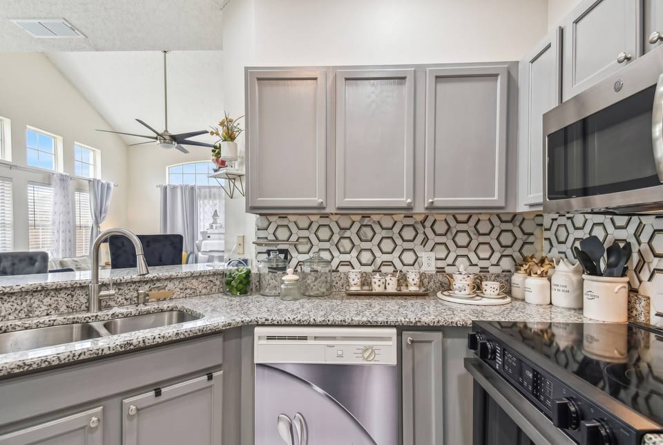 Experience a beautifully designed kitchen with sleek gray cabinetry and a modern backsplash. Spacious granite countertops inspire your culinary creativity, and the natural light creates an inviting atmosphere for your stay.