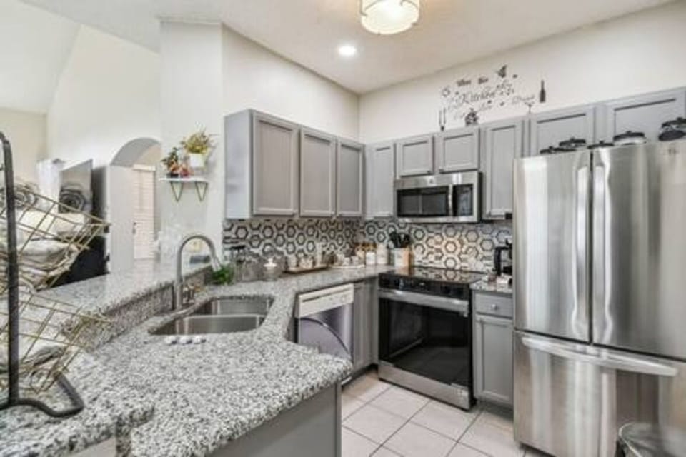 Experience a stylish kitchen featuring sleek gray cabinetry and a vibrant patterned backsplash. Enjoy spacious granite countertops for effortless meal prep and modern appliances that enhance your culinary adventures.