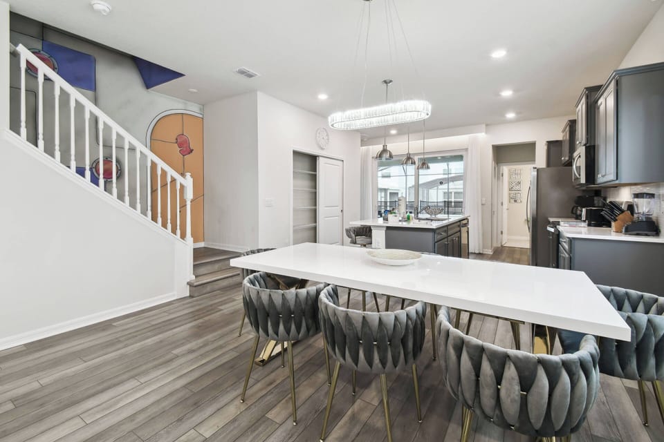 Enjoy the bright dining area with a sleek white table and stylish chairs, ideal for family meals or entertaining. Natural light enhances the modern kitchen, featuring dark cabinetry and a chic open layout.