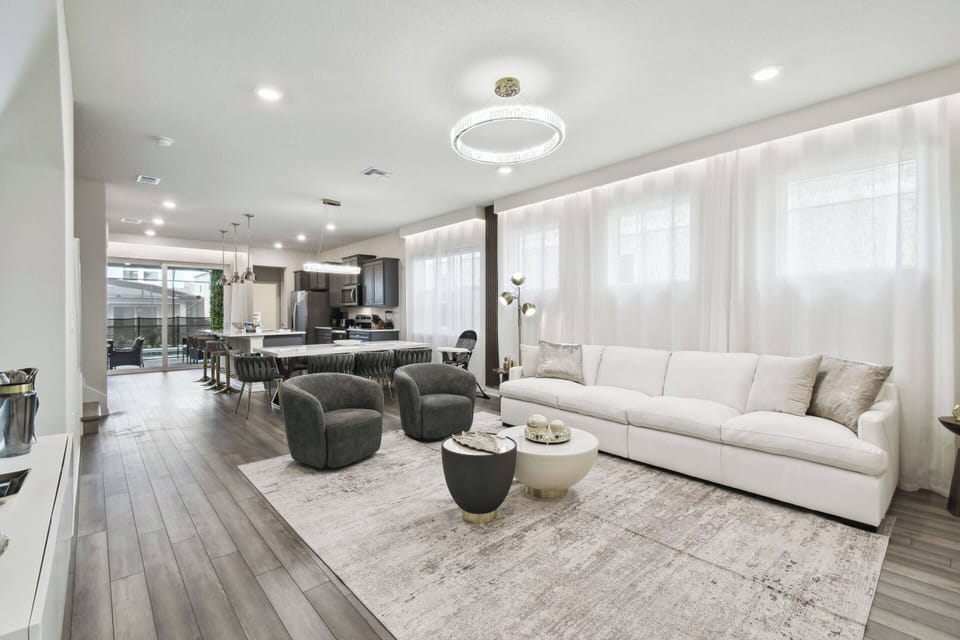 Enjoy a bright and airy living area with a plush cream sofa and chic dark accent chairs for relaxation. The warm wood flooring enhances the modern decor, and large windows fill the space with inviting natural light.