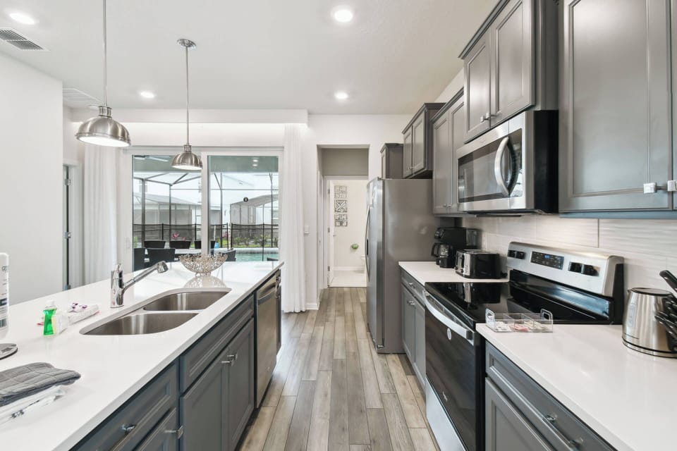 Experience a chic kitchen with dark cabinetry and bright quartz countertops, complemented by modern stainless steel appliances and ample lighting that inspire your culinary creativity, all enhanced by large windows letting in.