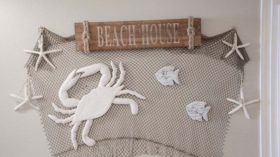 This whimsical décor features a rustic "Beach House" sign and fishing net with sea creatures, adding a playful coastal touch.