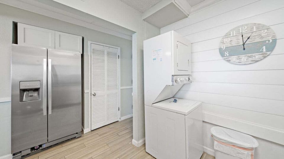 Convenient laundry area with stacked washer and dryer next to full-size fridge—perfect for extended stays. Clean, functional, and ready for beach towels or quick loads.