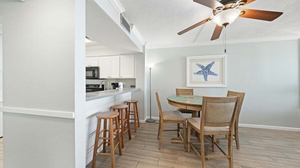 Open dining area with round table for four and breakfast bar with extra seating—perfect for meals, games, or planning your beach day. Coastal touches and natural light create a relaxed, inviting vibe.