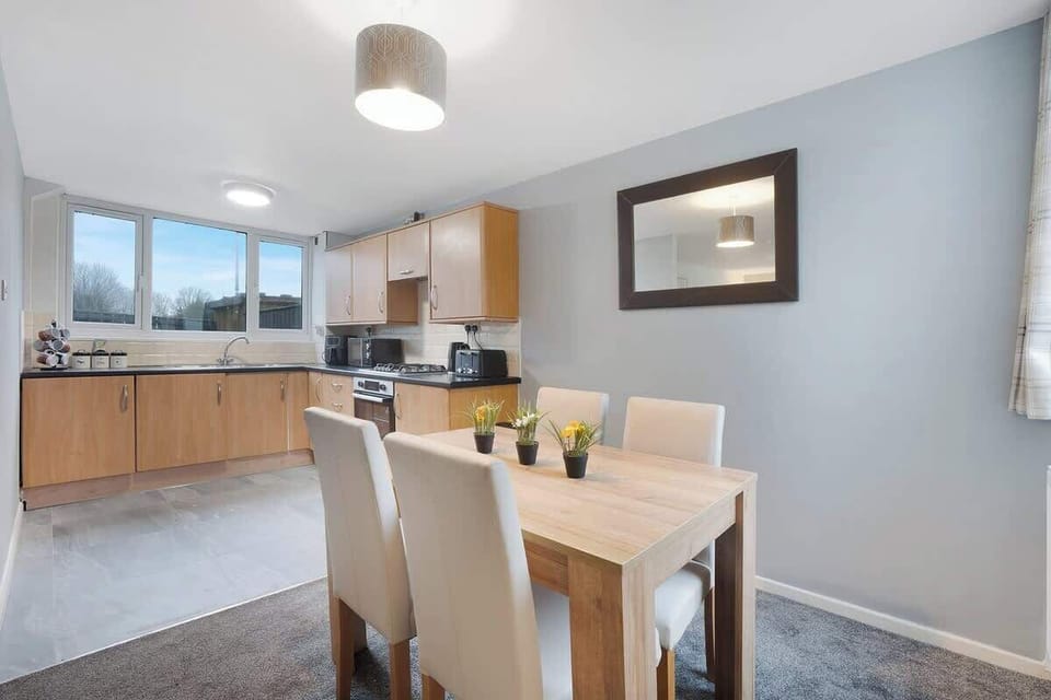The dining area, adjacent to the kitchen, features a rustic wooden table with seating for four. A stylish pendant light hangs overhead, providing a warm ambiance. Large windows let in natural light, while soft drapes add a touch of elegance. 