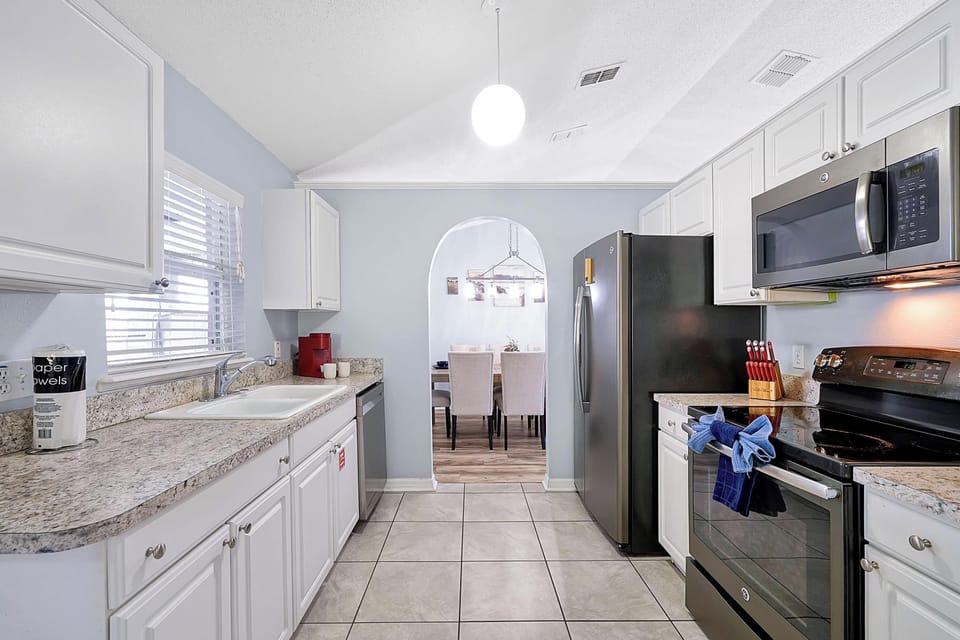 This modern kitchen features white cabinetry, granite countertops, and essential appliances, including a coffee maker. 
