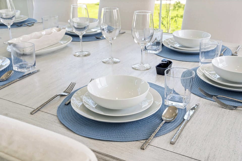 Bright dining area with seating for 8, surrounded by large windows and natural light. Features modern chandelier, coastal artwork, and direct access to the outdoor deck—ideal for family meals, game nights, or enjoying morning coffee.