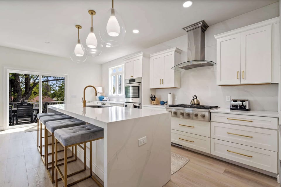 Fully equipped chef’s kitchen with quartz island, stainless steel appliances, double ovens, gas range, pendant lighting, bar seating, and direct access to the back deck for seamless indoor-outdoor dining.