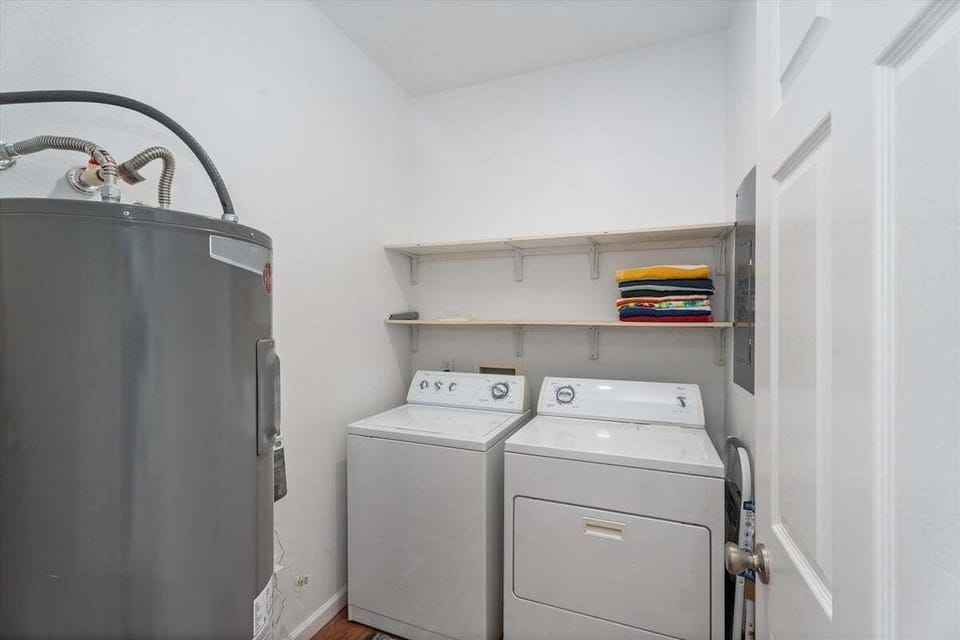 Dedicated laundry room with full-size washer and dryer, utility sink, water heater, open shelving and folded linens for convenient extended stays.