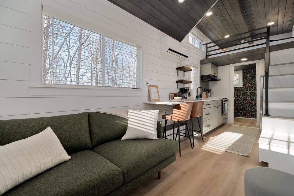 Hughes exterior — dark modern tiny home, personal hot tub on the deck, wooded surroundings at Notestone Reserve