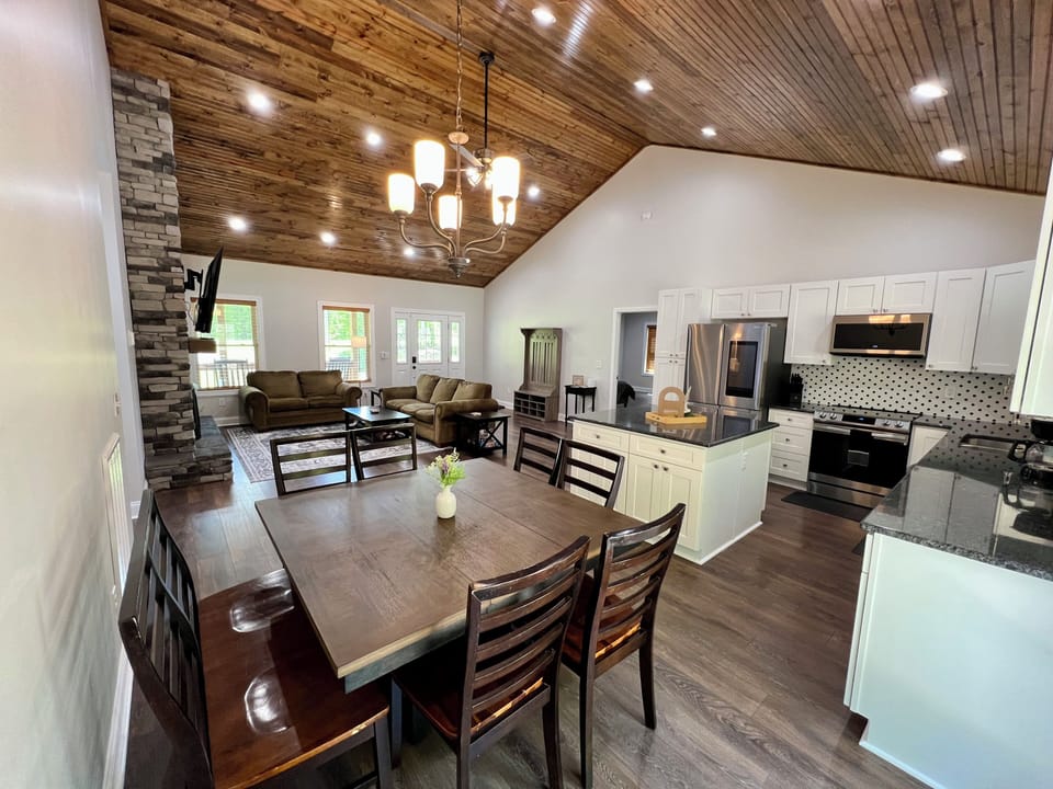 Open-concept living area with dining table and vaulted wood ceilings.