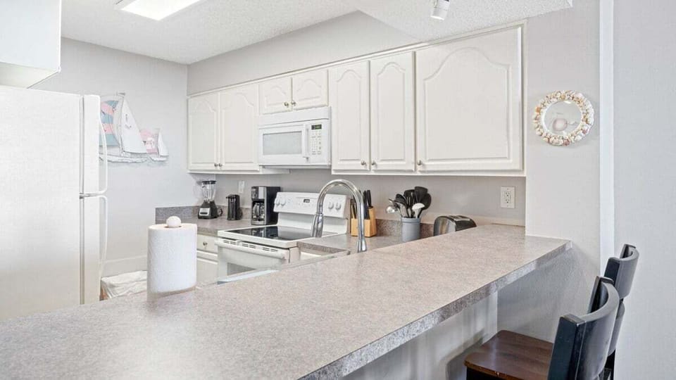 This kitchen offers bright white cabinetry, full appliances, ample counter space, and bar seating for casual meals.