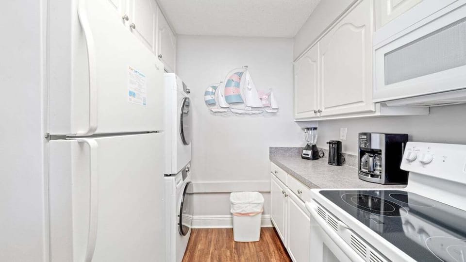 This bright kitchen features white cabinetry, modern appliances, essentials for cooking, and a stacked washer and dryer for convenience.