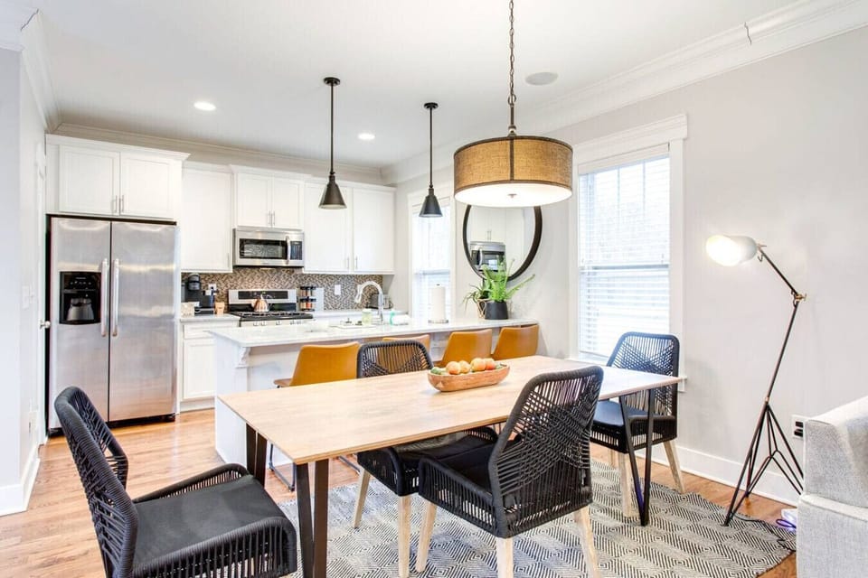Features a wood dining table with black woven chairs, leather barstools at a white island, and a light gray sectional sofa that converts into a Queen-sized bed. Stylish and modern throughout.