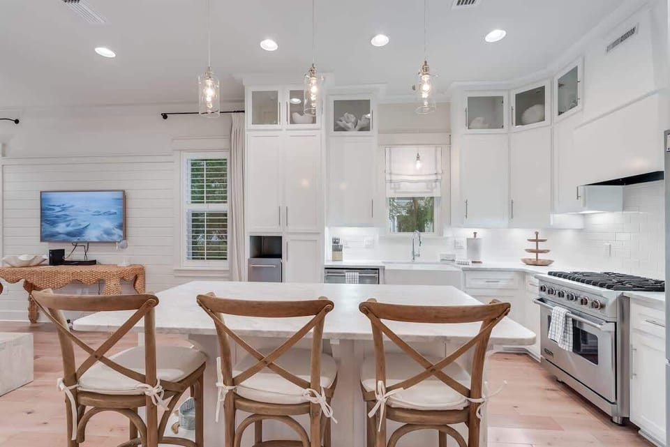 - Spacious kitchen with a cozy bar seating area and a view of the living room - Bright, modern design featuring white cabinetry and a large central island - Equipped with essential appliances and stylish pendant lighting for an inviting atmosphere