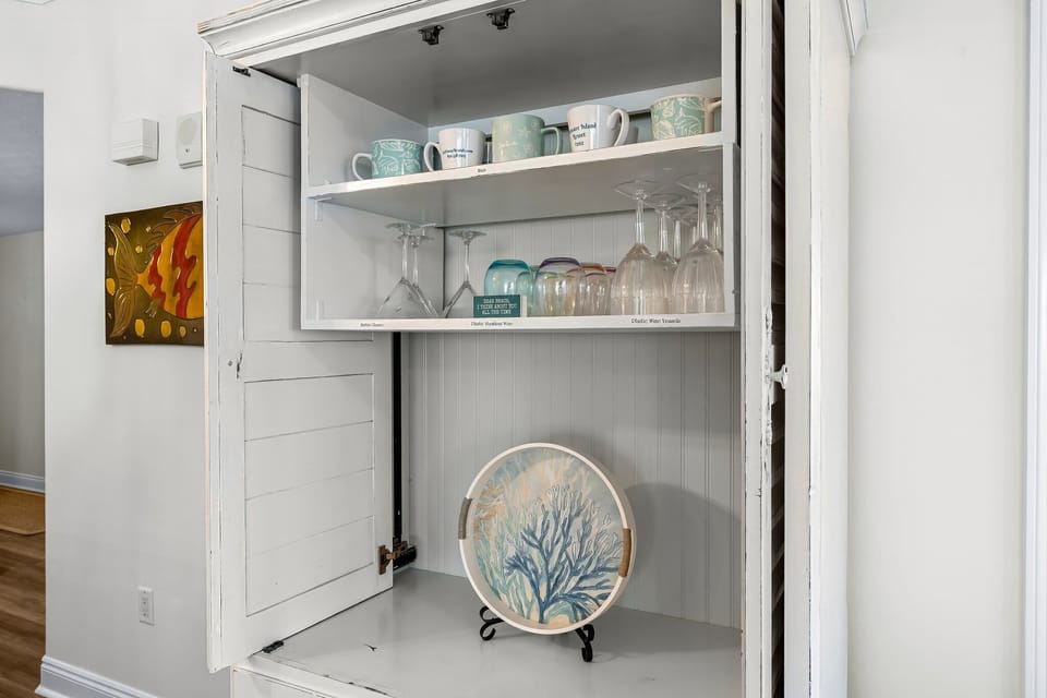 Open cabinet showcasing a collection of mugs, glasses, and a decorative plate in a bright kitchen.