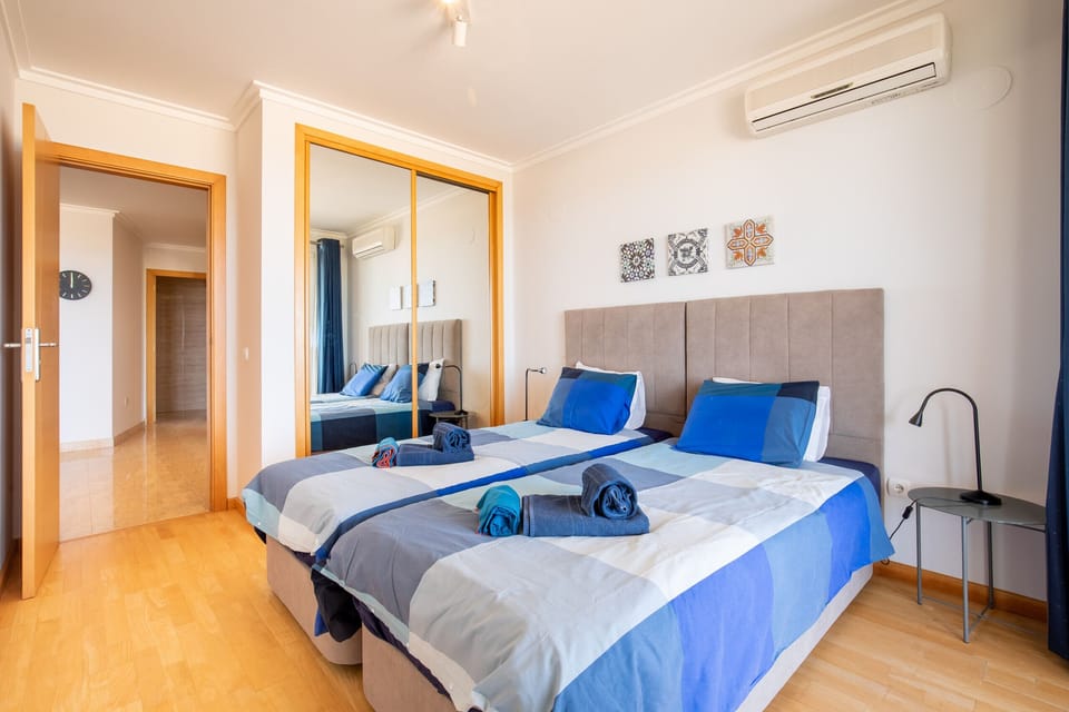 Spacious and bright bedroom with two single beds, ideal for couples or friends. It features a large mirrored wardrobe, air conditioning and blue tones that create a calm holiday atmosphere. A comfortable and functional space to relax after a beach day.