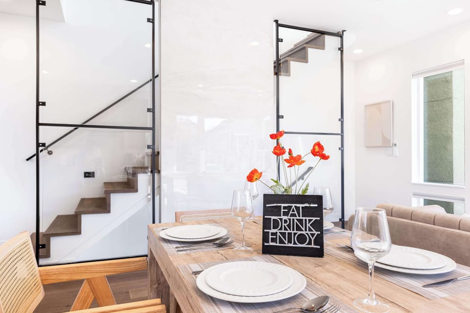 The photo captures the dining table, a welcoming living room with cozy seating, and a sleek staircase leading to the second floor, all arranged for comfort and style.
