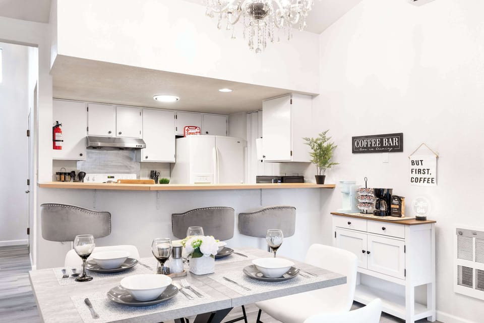 The open kitchen design is complemented by a modern dining table set for four. With a charming coffee bar nearby and elegant lighting, this space is both functional and stylish for any guest.