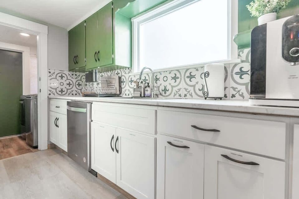 A modern kitchen with green cabinets and tiled backsplash, adjacent to a practical laundry area with essential amenities.