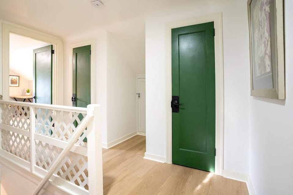 An elegant upstairs hallway with a bright and airy design. The hallway connects to multiple rooms through vibrant green doors, with a charming lattice railing adding a touch of character.