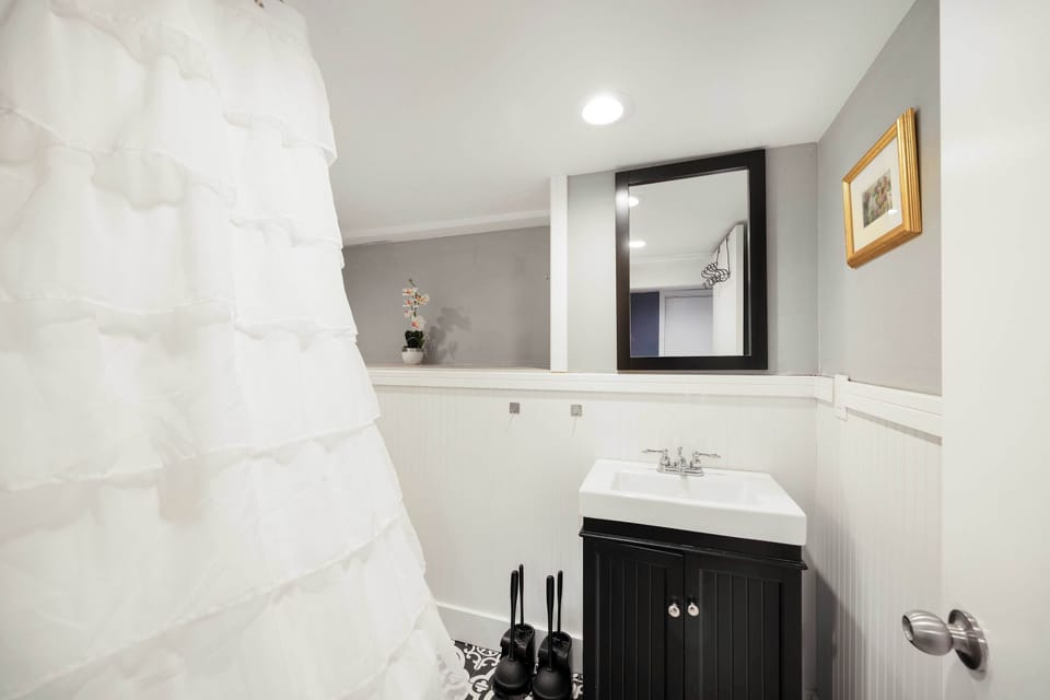 A sleek bathroom with a black vanity, a white ruffled shower curtain, and modern fixtures.