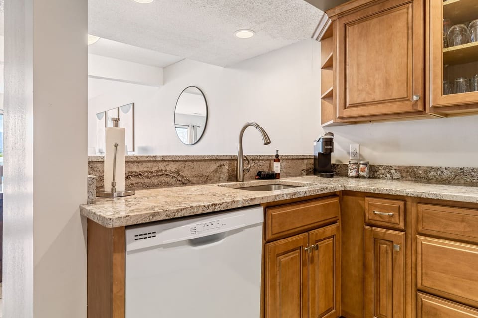 Close kitchen view of the sink, dishwasher, counter workspace, and single-serve coffee maker.