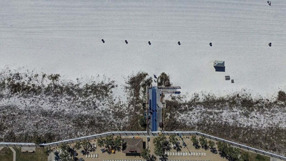 This overhead view shows a scenic boardwalk leading from a beachfront resort through natural dunes to the soft white sands and shoreline—your direct path to paradise.