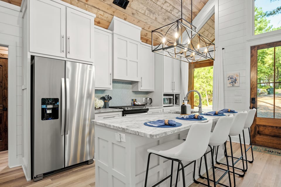 Sleek and modern kitchen with marble island, white cabinets, silver fridge.