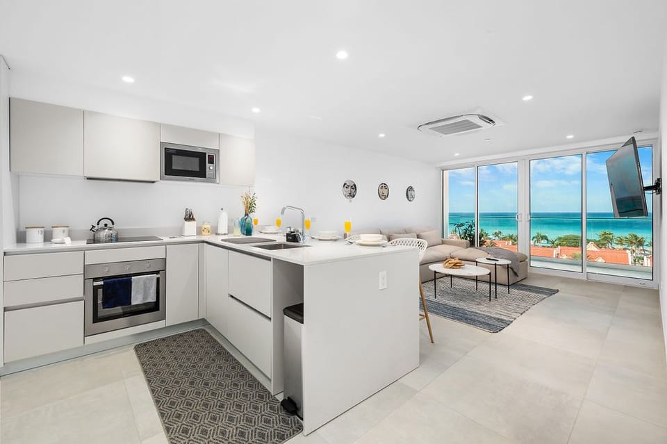Wake up to stunning ocean views from your modern, light-filled living space. The open-plan kitchen flows seamlessly into the living area, perfect for sipping morning coffee while turquoise waters sparkle beyond the glass doors.