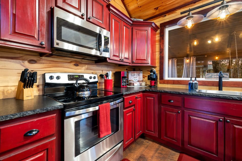 The cabinets are a vibrant red, complemented by black countertops and a rustic backsplash.