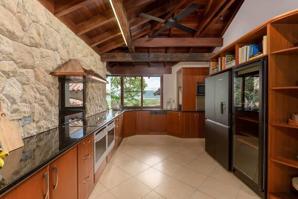 Create culinary masterpieces in this stunning kitchen, featuring a Bali marble accent wall, sleek granite countertops, double ovens, and rich timber cabinetry, all framed by lush tropical views.