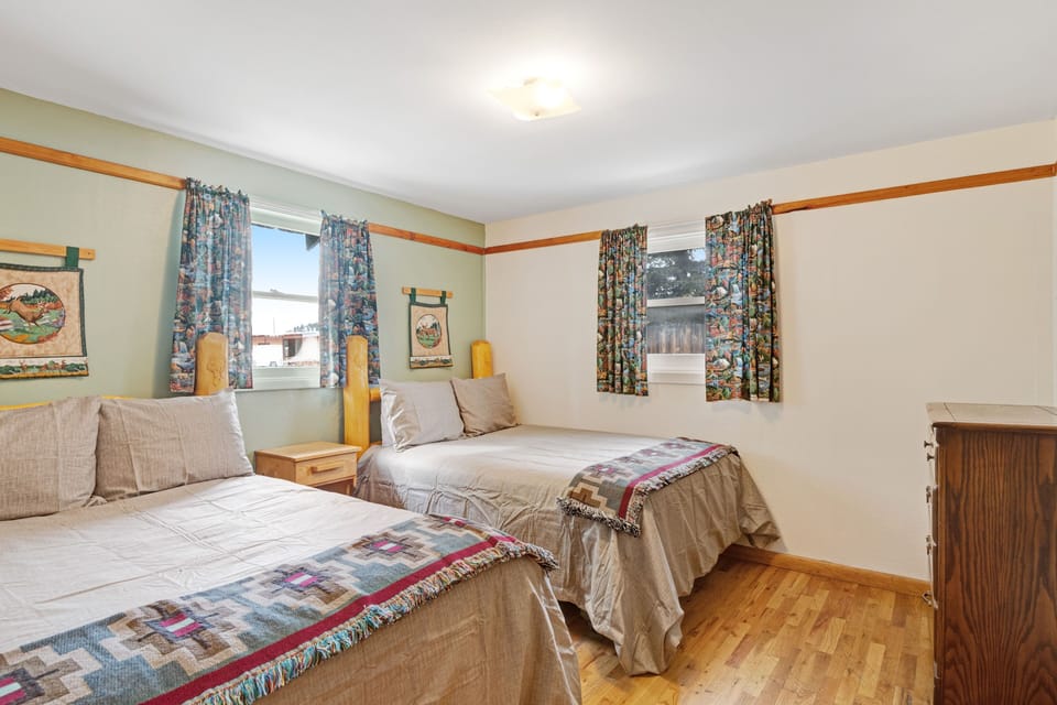 Bedroom with two beds, wood flooring, and patterned curtains.