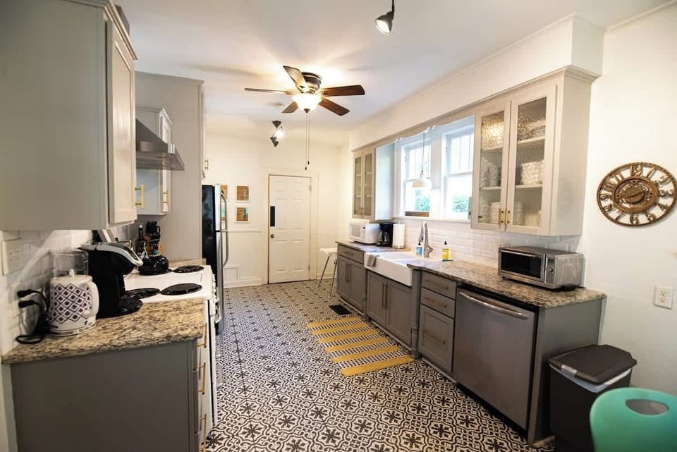 Prepare meals in this spacious, fully equipped kitchen featuring granite countertops, grey cabinetry, stainless steel appliances, a farmhouse sink, and stylish patterned tile flooring.