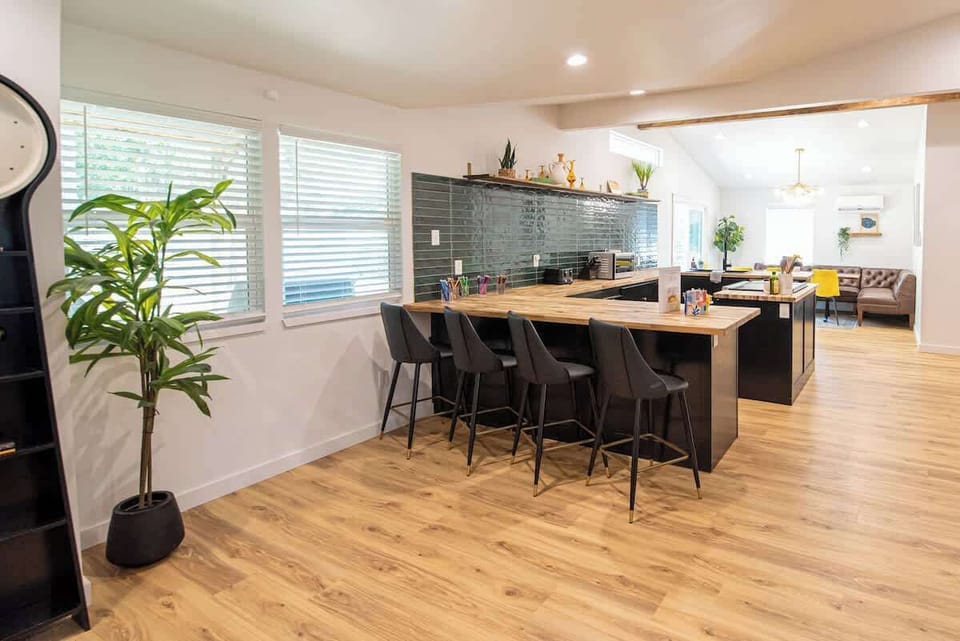 Gather and entertain around this modern kitchen island, featuring sleek black barstools, butcher block countertops, deep teal subway tile backsplash, and an open layout flowing effortlessly into the dining area.