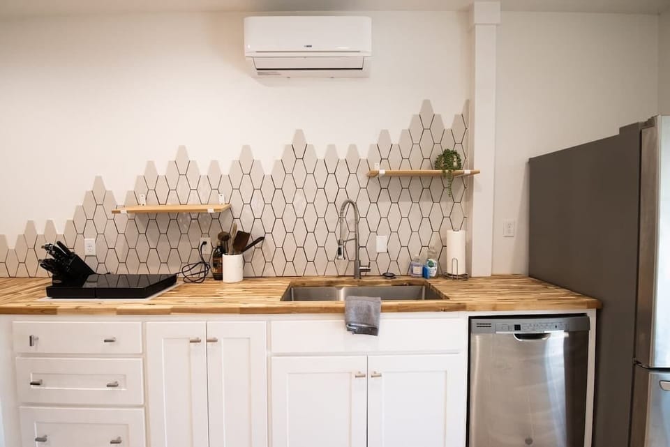 Enjoy cooking in this stylish kitchen complete with a stainless steel sink, butcher block countertops, white cabinets, and a unique geometric tile backsplash.